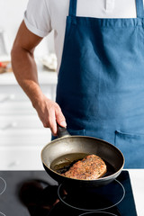 partial view of man holding pan with cooked steak