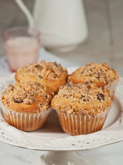 Top view, close distance of four, freshly baked, homemade peanut crumb chocolate chip muffins on a round, white, pedestal display dish with a glass  of milk and a milk pithcer