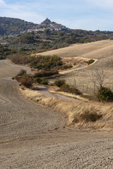 The curved country road through arable fields to the medieval castle-town in Tuscany, Italy