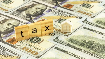 Wooden block and a small home model on dollar bills. Tax Concept.