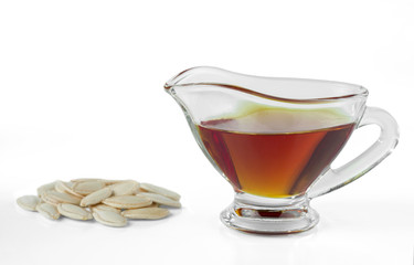 Pumpkin oil in a glass gravy boat and pumpkin seeds isolated on white background.