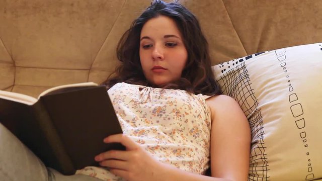 Teenager Girl reads a book on comfy sofa