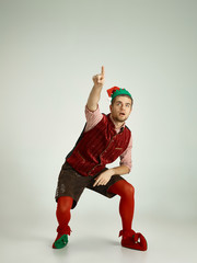 The happy smiling friendly man dressed like a funny gnome or elf pointing up on an isolated gray...