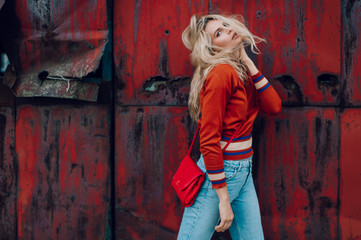 Lifestyle fashion portrait of young beautiful cute girl model.  Odd bizarre strange unusual cute naughty blonde babe posing on old rusty metal gate background. Nice looking woman in trendy clothes.