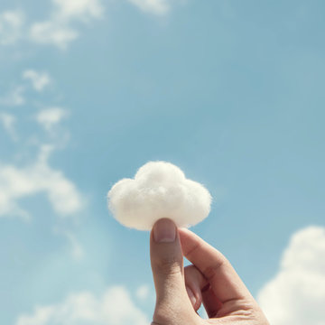 Woman hand holding cotton wool on cloud sky background. The development of the imagination, copy space.