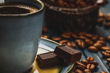 Cup of coffee on a blue wooden table with coffee beans and a chocolate.