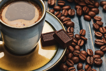 Cup of coffee on a blue wooden table with coffee beans and a chocolate.