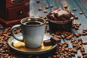 Cup of coffee on a blue wooden table with coffee beans and a chocolate