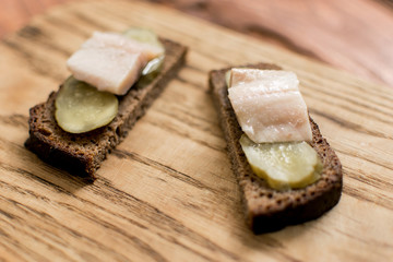 Sandwich from black bread with butter and herring on a wooden background.