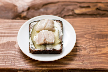 Sandwich from black bread with butter and herring on a wooden background.