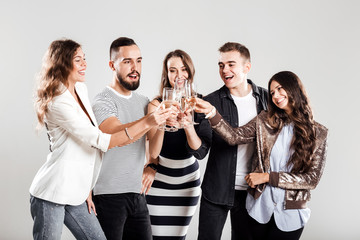 Girls and guys dressed in stylish casual clothes stand together and clink glasses with champagne. Party time