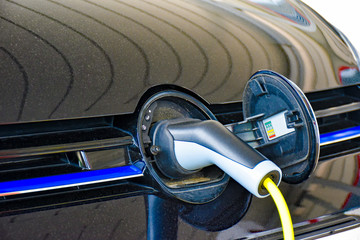 A electric vehicle is charged at a charging station. The charging plug is plugged into the socket hidden behind the brand logo.
