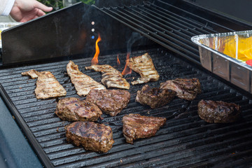Rindfleisch und Speck brutzeln zwischen züngelnden Feuerflammen auf dem Gas Grill