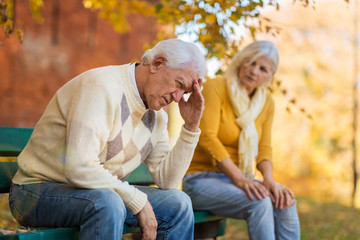 Senior man suffering from a headache, senior woman comforts him