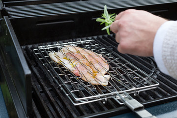Mann garniert den Grillfisch im Grillgitter mit Thymian