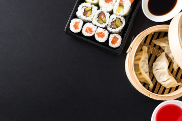 Dumplings or gyoza served in traditional steamer and sushi on black background. Top view. Copyspace