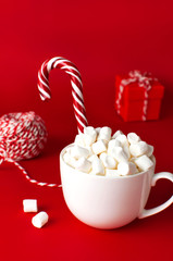 White mug with marshmallows Candy Cane gifts boxes packaging lace flashlight on red background Flat Lay copy space. Winter traditional drink food. Festive decor celebration Christmas New Year holiday