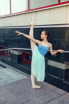 Ballet dancer dancing on street. Young ballerina in color tutus. Ballet feet on the point. Pretty ballerina near the theater doing exercise.