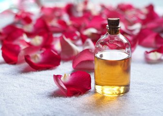 Obraz na płótnie Canvas Aroma oil glass bottle among red rose petals on white terry towel. SPA and relax concept, selected focus