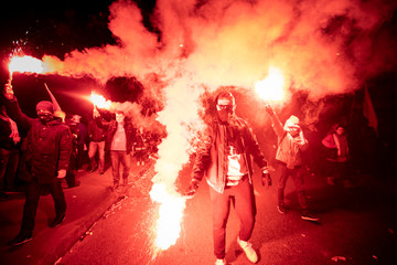 People carry Polish flags and burn flares as they walk across the Poniatowski Bridge during a march...