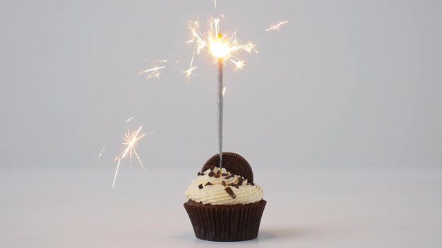 Delicious birthday cupcake with burning sparkler on white table