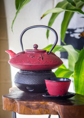 red zen tea pot sitting on wooden table great for relaxing, happiness, joy and mindfulness. green house plant sits behind tea