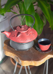 Obraz na płótnie Canvas red zen tea pot sitting on wooden table great for relaxing, happiness, joy and mindfulness. green house plant sits behind tea