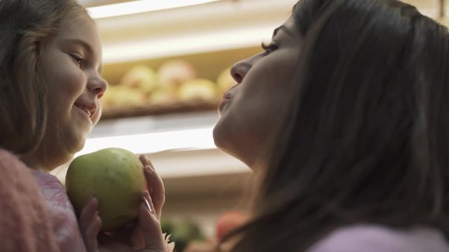 Mom gives an apple to her little daughter and kisses her