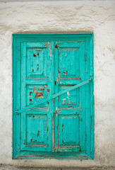 Old wooden shutters of turquoise color, paint cracked, closed with an iron crossbar. Background, white dirty wall