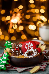 Gingerbread mittens, little man, snowflakes, christmas trees in a brown wooden plate and a bottle of milk on a green wooden on the background of blurred garland. close up. space