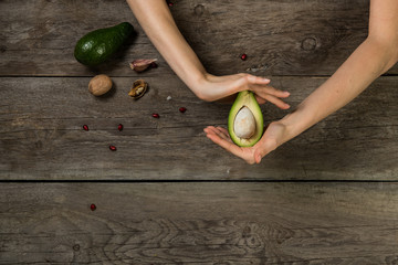 Woman hands gently holding half-cut piece of avocado above wooden background