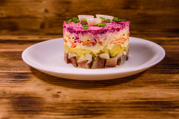 White plate with russian traditional new year salad herring under fur coat on wooden table