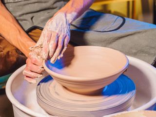 Creating earthenware and traditional pottery concept. Experienced male potter's hands creating beautiful clay product - bowl - using professional tools. Toned cinematic, craft factory authentic