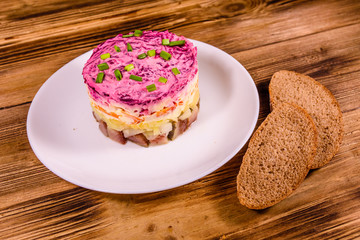White plate with russian traditional new year salad herring under fur coat and rye bread on wooden table