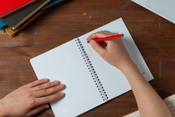 Female hand writing on notepad sheet placed on woode desktop with keyboard. She is doing paperwork. Working women holding a pencil writing a notebook.