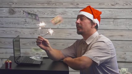 dreamy man in a christmas hat with bengal fire sparkler and laptop in his hands. Falling Money Dollars.