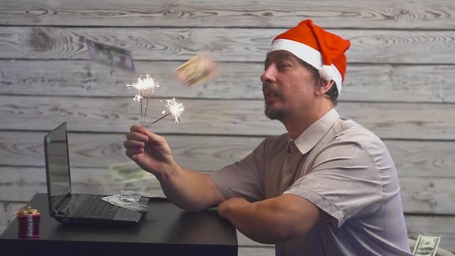dreamy man in a christmas hat with bengal fire sparkler and laptop in his hands. Falling Money Dollars.
