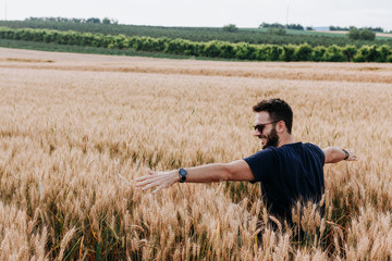 Naklejka na ściany i meble Young man in the wheat field with spread arms 