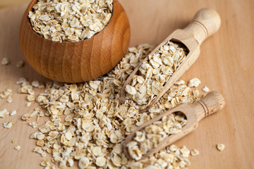 Oat flakes in a wooden bowl with a scoop on the wooden board