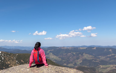 Fototapeta premium A girl with a backpack sitting on a large rock in the mountains. The concept of travel