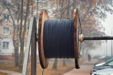Black wire electric cable with wooden coil. Emergency work on laying the power and communication cable under the ground. Stand for wire uncoiling.