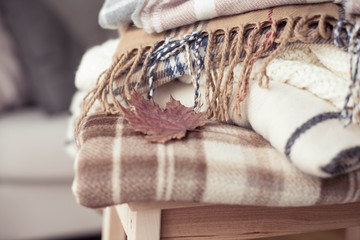 Fototapeta na wymiar Blankets close up. Autumn cozy interior. A stack of warm blankets lie on a wooden chair. Autumn. Winter.