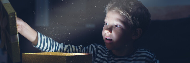 Wide view retro image of surprised toddler boy opening a golden gift box