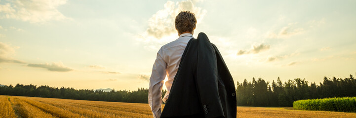 View from behind of a businessman standing in nature under evening sky