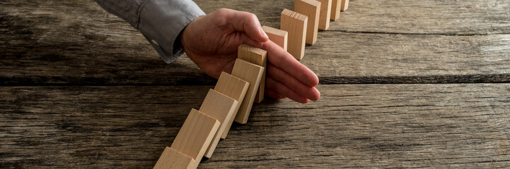 Wide view image of businessman stopping domino effect - obrazy, fototapety, plakaty