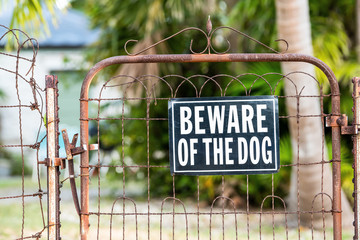 Beware of the dog sign on closed rusty fence gate with rust at residential neighborhood with house,...