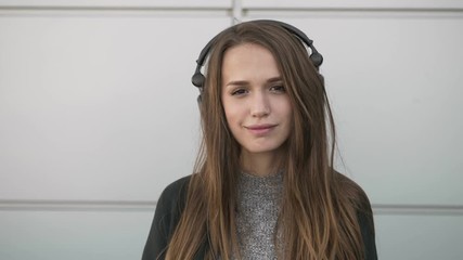 Close up slow motion young stylish long hair brunette woman big dj headphones enjoying music dancing, smiling on the wind metal panels city wall - Powered by Adobe