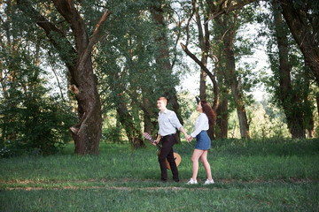 Naklejka premium young couple walking in the forest and playing guitar, summer nature, bright sunlight, shadows and green leaves, romantic feelings