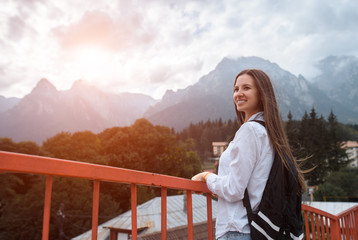 Fototapeta na wymiar Smiling hipster girl with backpack on background of mountains