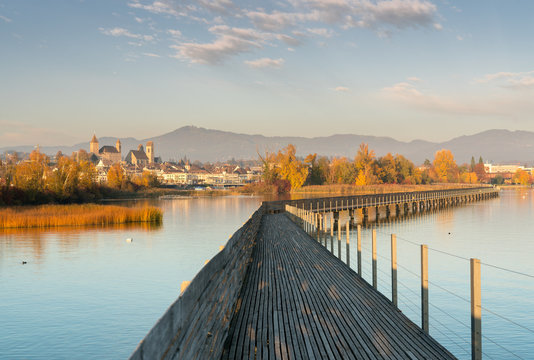 landscape view of marsh and lake shore with the town of Rapperswil in evening light and along wooden boardwalk in the foreground